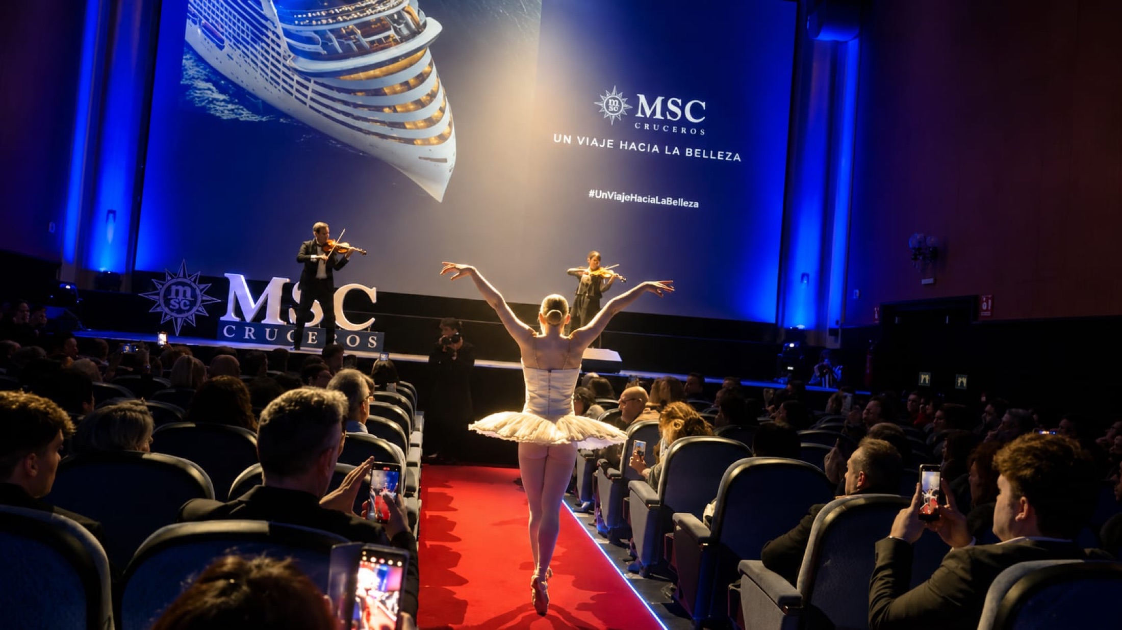 Bailarina en un pasillo rojo, ante una pantalla de presentación.