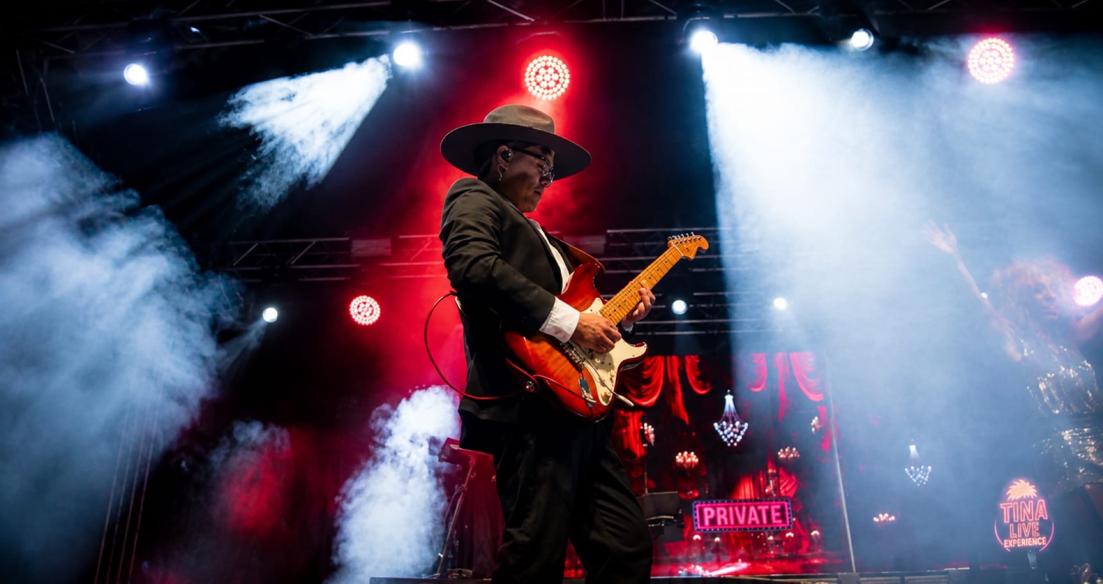 Guitarrista en un escenario con humo y luces rojas.